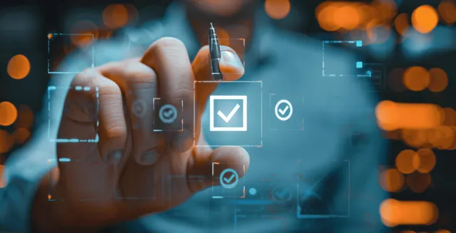 Hand with pen ticking a digital quality checklist beside approval icons on blurred office backdrop