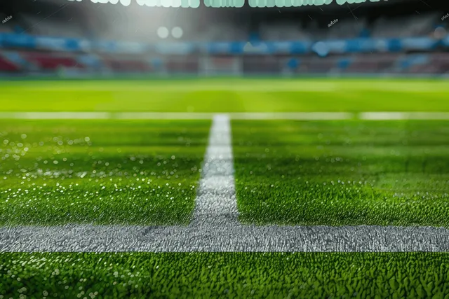 Green soccer field with a white center line stretching toward blurred stadium stands.