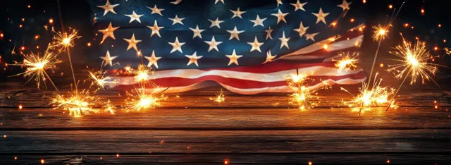 American flag waving behind sparklers on wooden table, fireworks sparks and warm bokeh