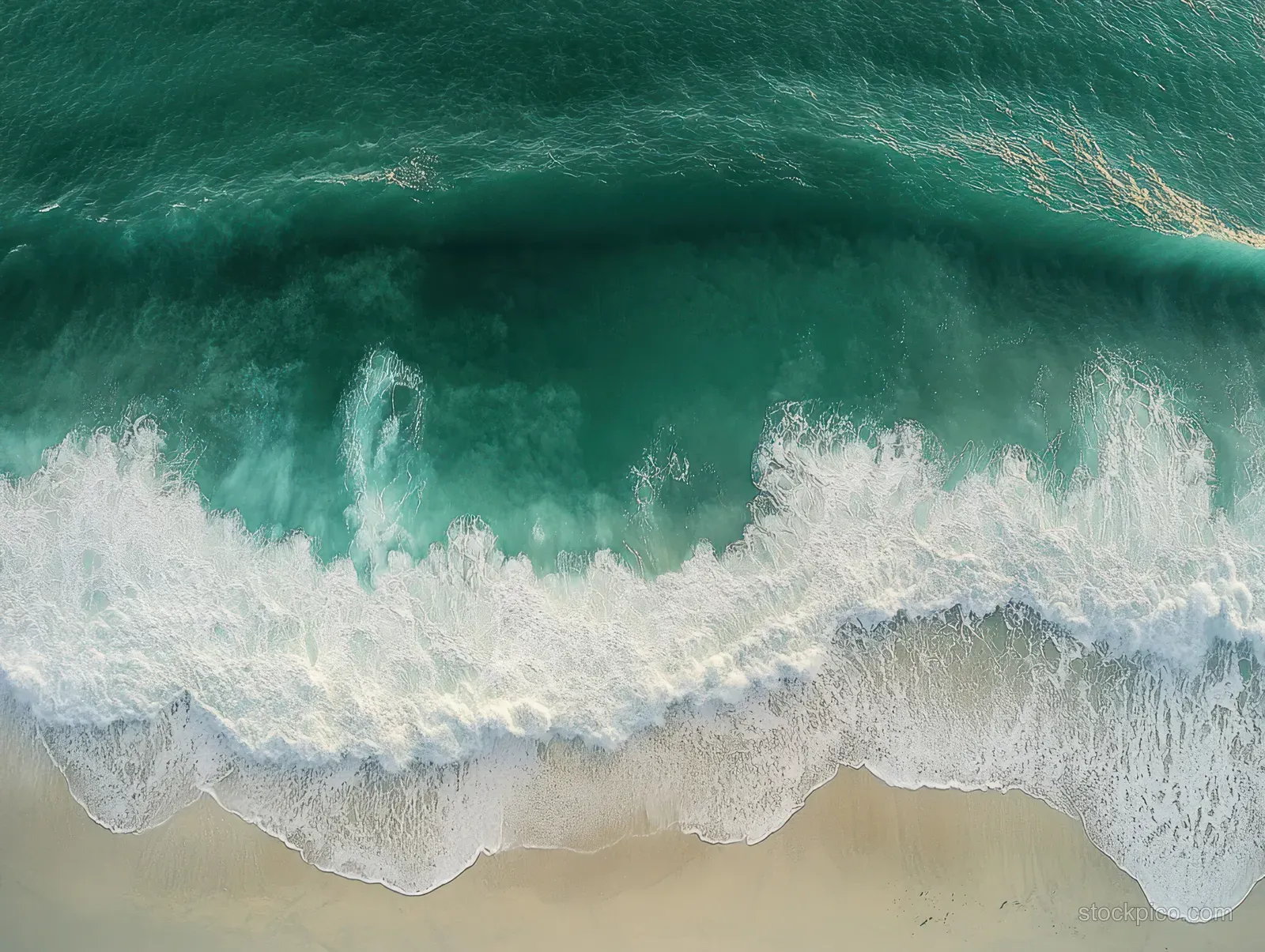Aerial view of turquoise waves breaking onto a sandy beach with white foam.