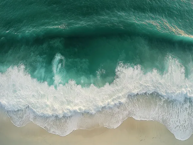 Aerial view of turquoise waves breaking onto a sandy beach with white foam.