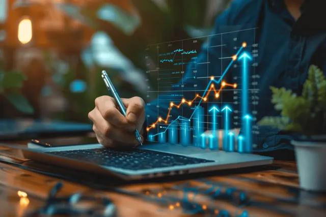 A woman writes next to a laptop showing rising bar and arrow graphs for business growth analysis.