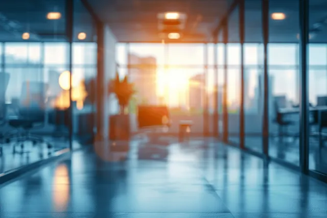 Sunlit modern office corridor with panoramic windows and warm bokeh blur across the floor.