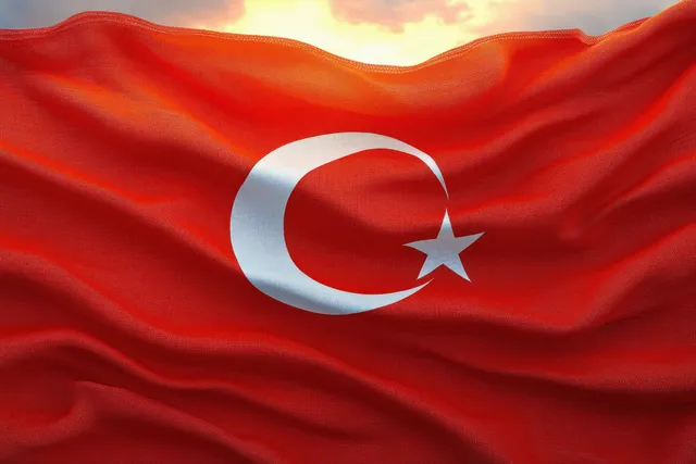 A red flag waves with a white crescent moon and star in the sky at sunset.