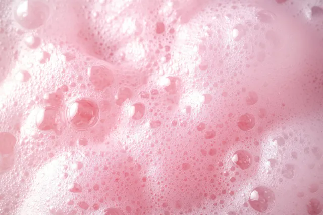 Macro pink soap foam bubbles spread over a soft pastel surface, creating a fresh hygiene texture.