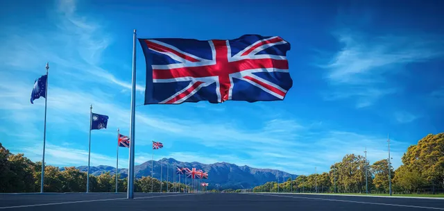 New Zealand national flag waving on tall pole under bright blue sky with clouds