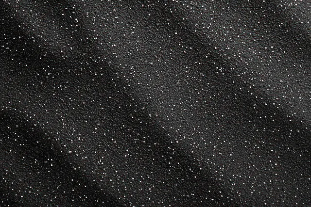 Textured black surface with scattered white specks, starry abstract background