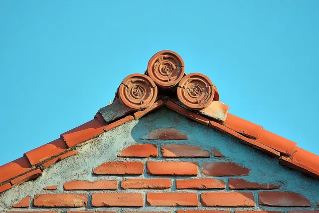 A triangular brick wall with three circular terracotta roof tiles sits against a clear blue sky.