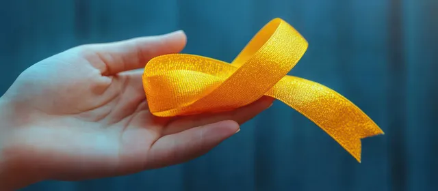Una mano sostiene una brillante cinta amarilla de concienciación sobre un fondo azul desenfocado.