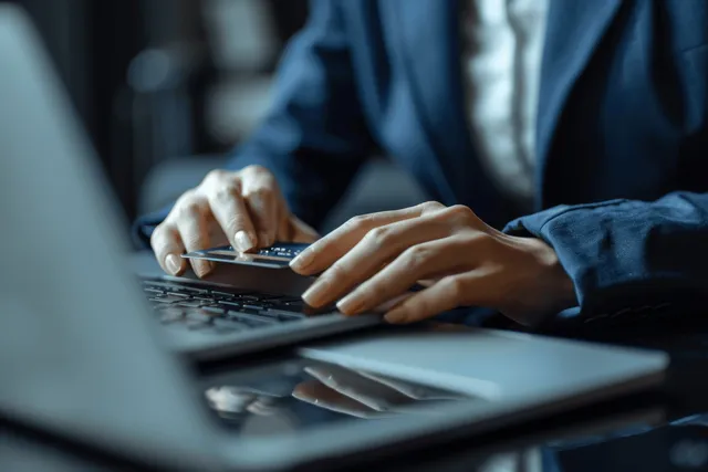 Businesswoman paying online with smartphone and laptop at office desk, credit card visible
