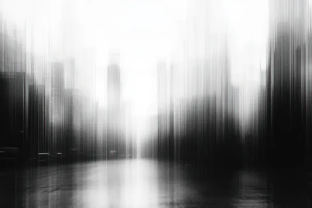 Monochrome blurred city street recedes past tall skyscraper silhouettes under a hazy sky.
