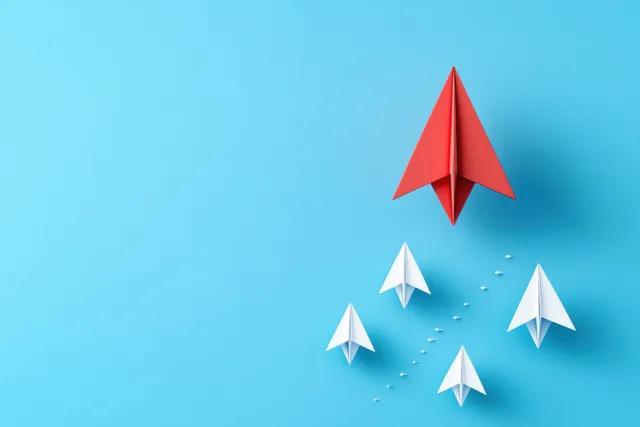 Red paper airplane leading upward above white paper planes on blue gradient background