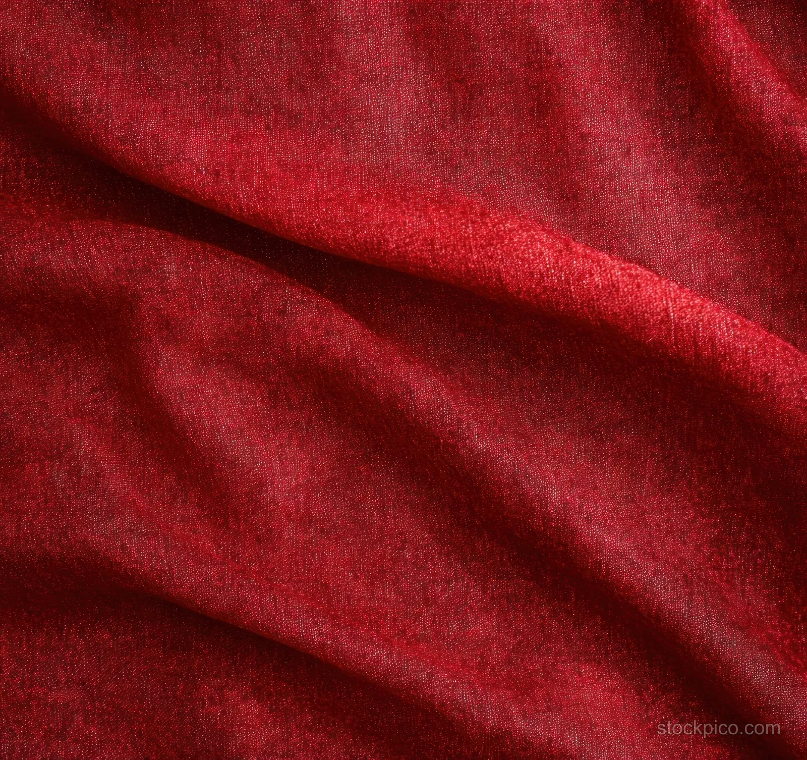 Soft red textured fabric close-up with gentle folds and shadowed creases.