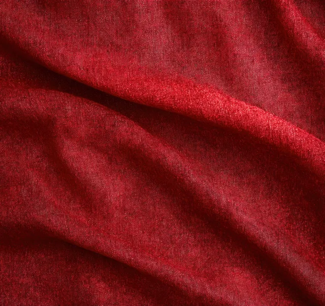 Soft red textured fabric close-up with gentle folds and shadowed creases.