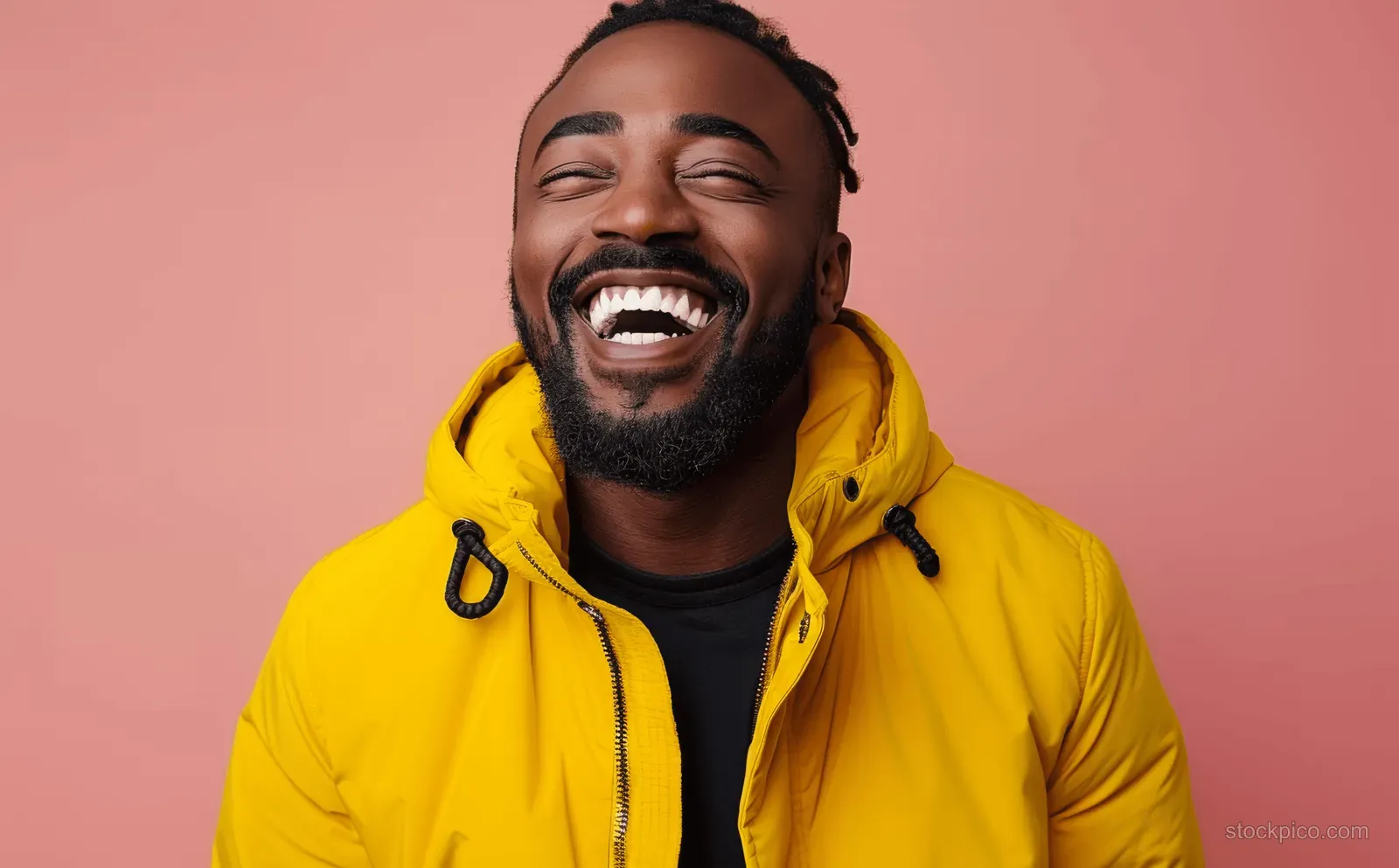 Laughing young Black man in a yellow hoodie smiles against a smooth pastel pink background.