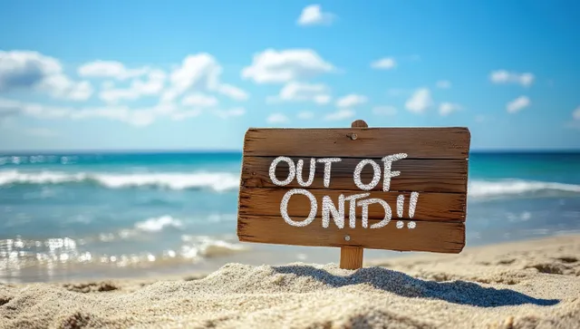 Weathered wooden sign stuck in beach sand facing the ocean under blue sky