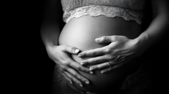 Monochrome close-up of a pregnant mother’s hands cradling her belly under soft diffused light.