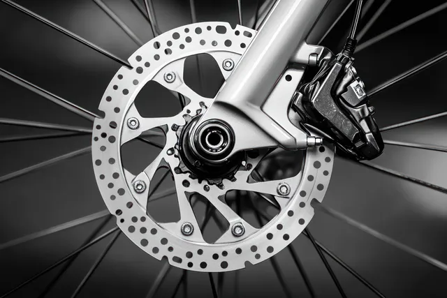 Close-up of a bicycle disc brake rotor and caliper with metallic spokes and blurred wheel background.