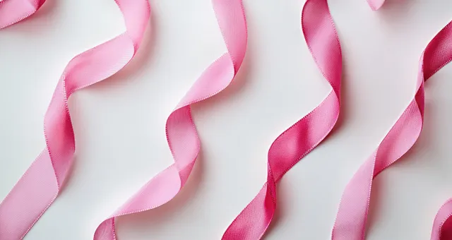 Pink breast cancer awareness ribbons curled on a white background under soft natural lighting.