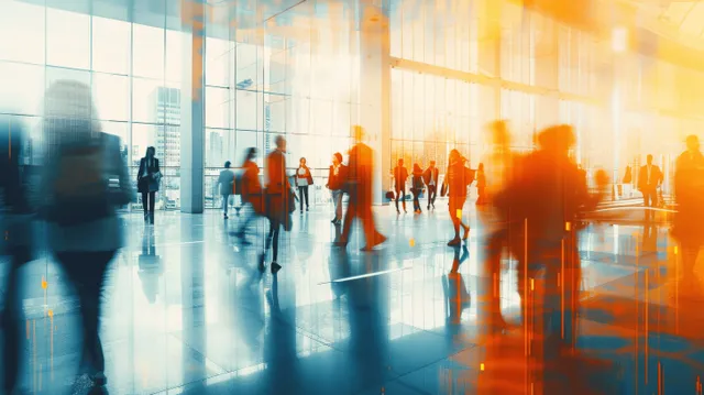 Blurred employees walk through a bright office lobby with panoramic windows and strong daylight.