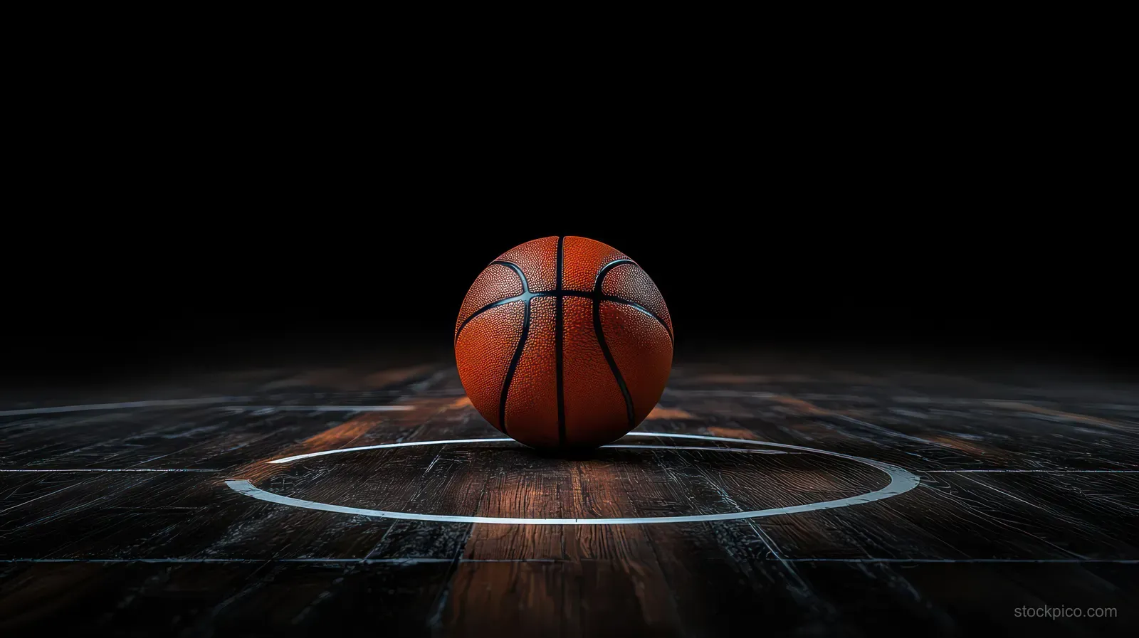 Basketball resting on a wooden indoor court floor within the three-point line under a dark background.