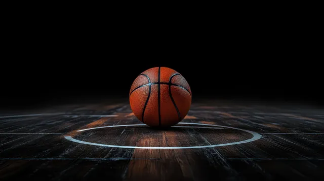 Basketball resting on a wooden court inside the three-point line, lit against darkness