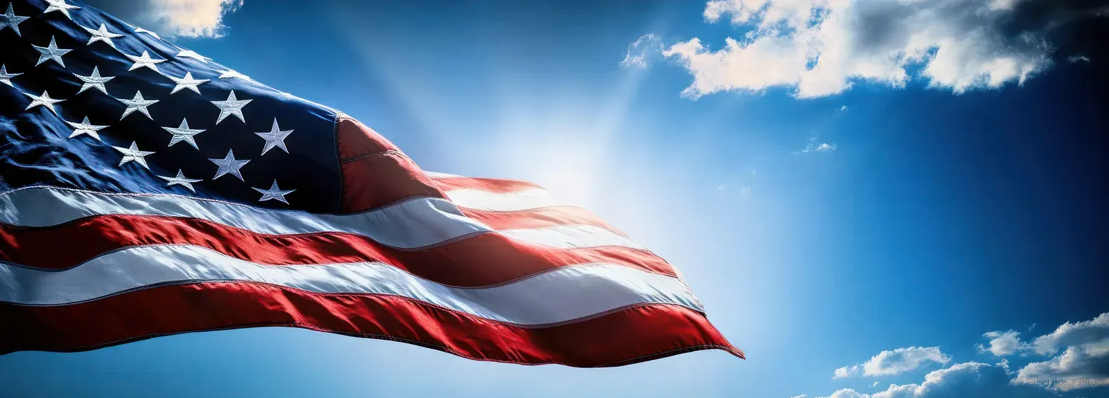 American flag waving in the wind against a bright blue sky with dramatic clouds.