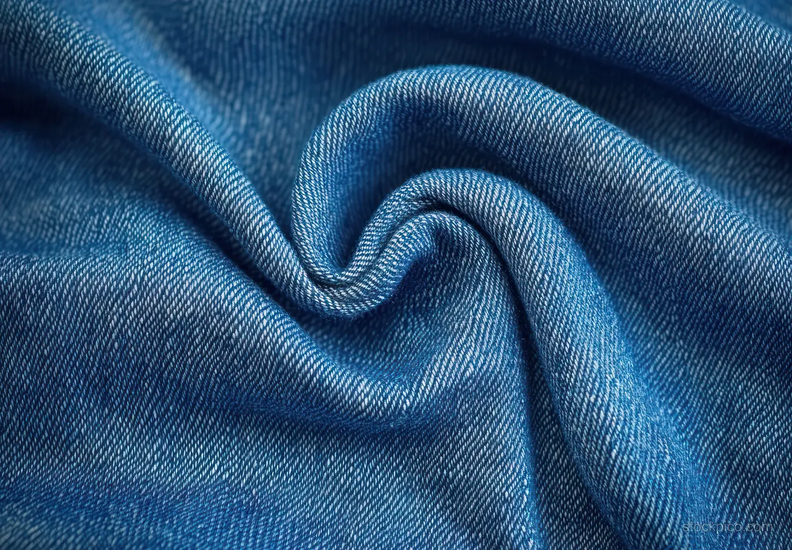 Twisted blue denim fabric close-up with detailed weave texture and folded creases.