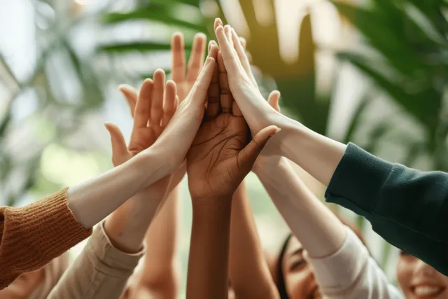Diverse team high-fives in a bright office, hands stacked in celebratory teamwork moment