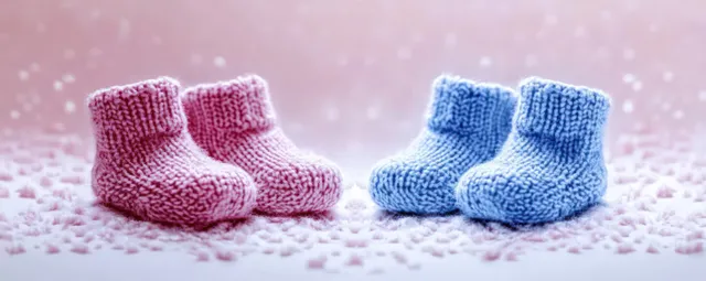 Blue and pink knitted baby booties resting on pastel fuzzy surface