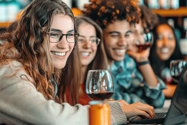 Smiling diverse students studying together at library tables with laptops and books