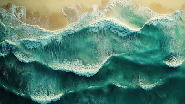 Aerial waves crash onto a sandy shore, turquoise water with white foam patterns