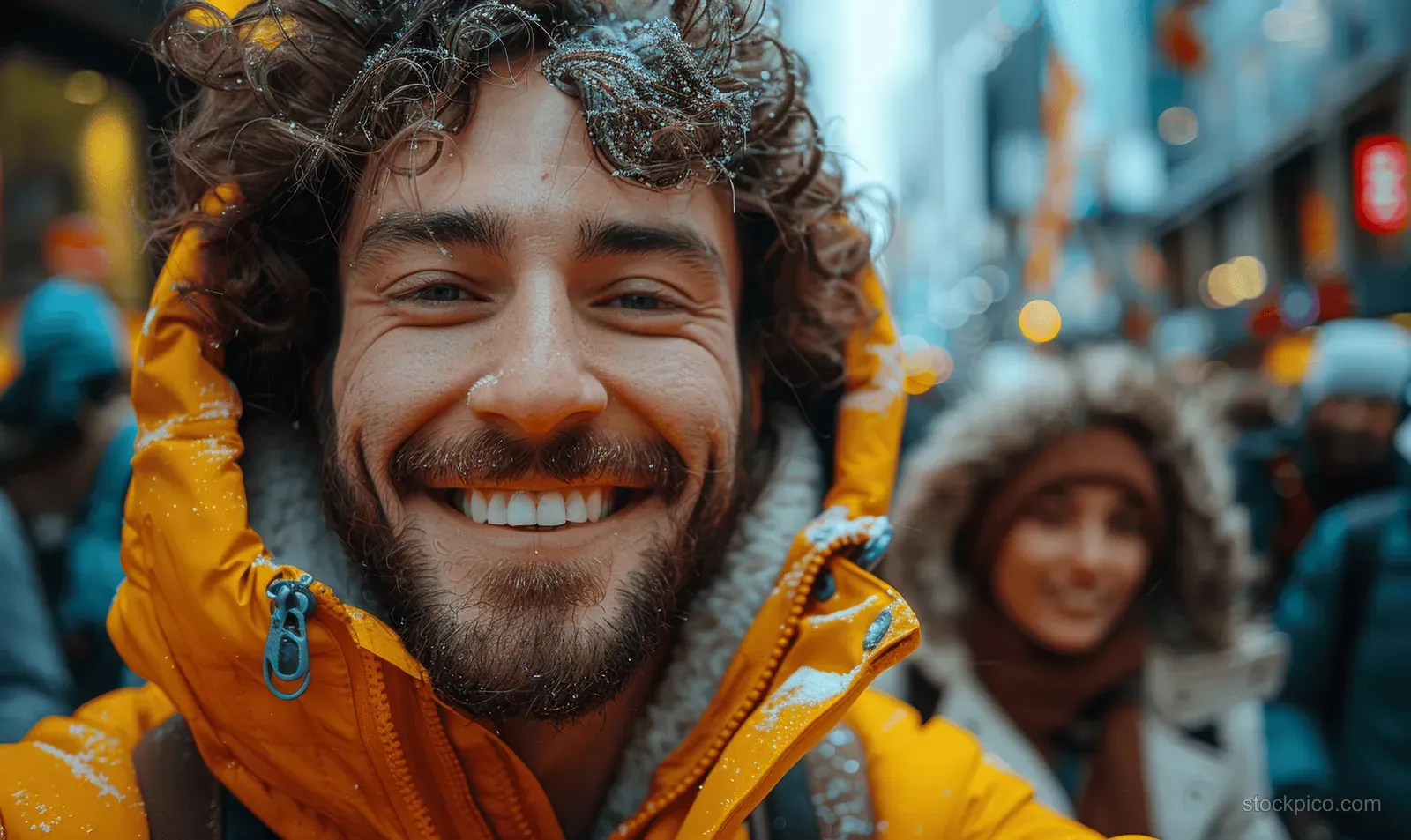 Young friends pose for a selfie on a city street with bright jackets and a blurred crowd behind them.