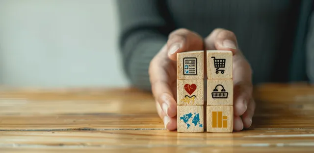 A person’s hands stack small building blocks with health and lock icons suggesting employee benefits security.