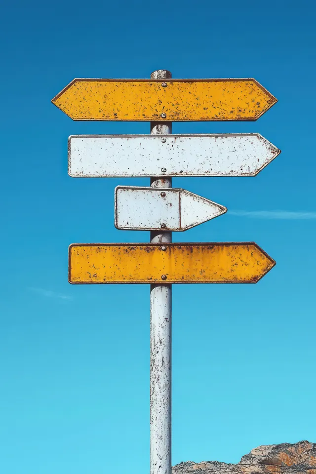 Rusty yellow and white arrow direction signpost against bright blue sky