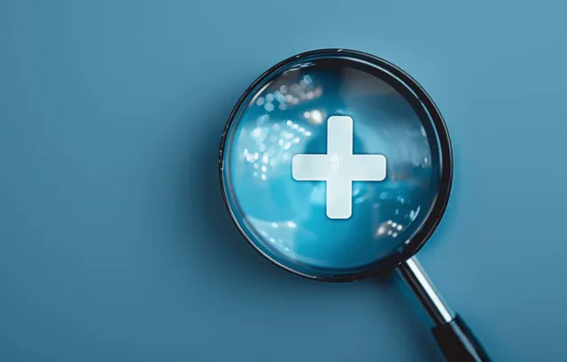 White medical plus sign inside magnifying glass on blue healthcare background