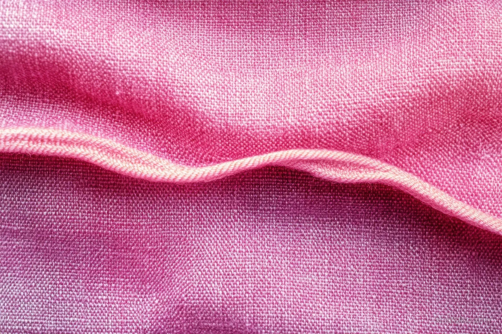 Soft pink fabric close-up with a flowing fold and visible woven texture under side lighting.