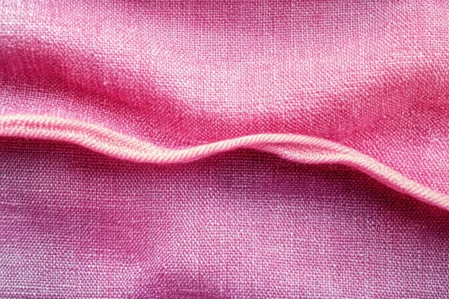 Soft pink fabric close-up with a flowing fold and visible woven texture under side lighting.