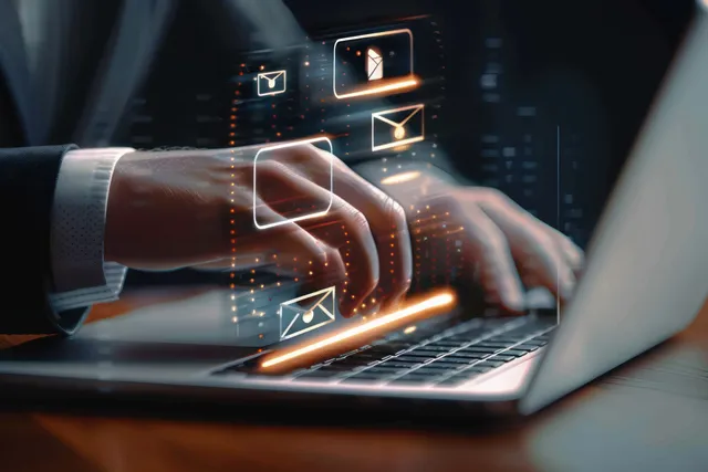 Hands typing on laptop keyboard with glowing email icons in dark workspace