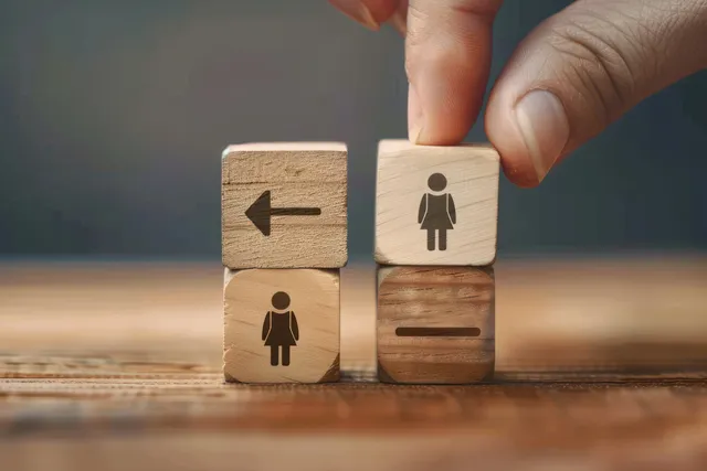 Hand places a wooden female restroom symbol block next to a block with a left arrow on a wood surface.