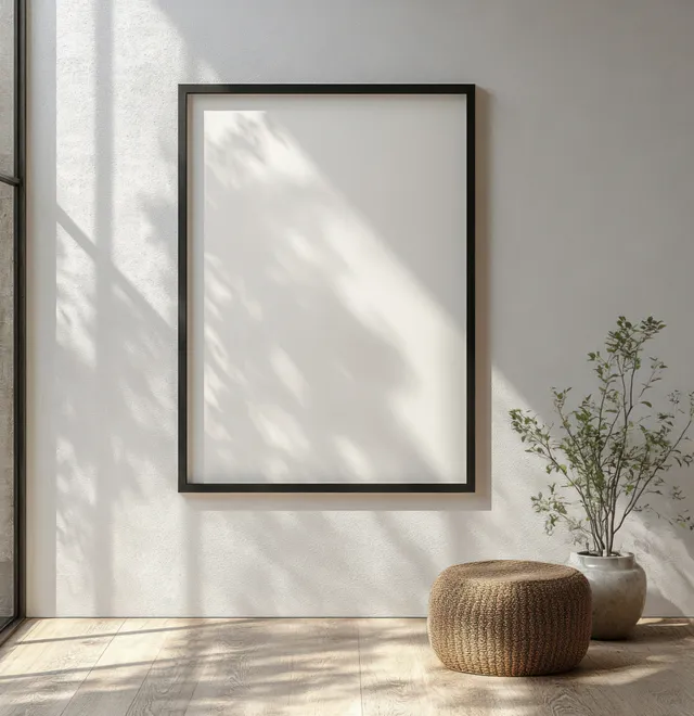 A minimalist black frame rests on a light wall, softly illuminated by natural light, providing space for custom artwork.