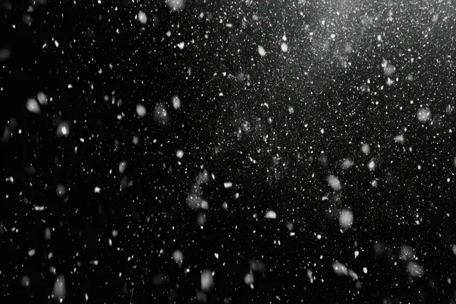 Close-up view of white snowflakes falling against a dark night sky with sparkling icy particles.