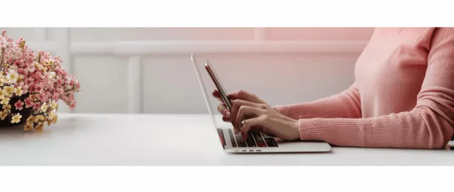 Woman typing on laptop while using smartphone at bright white desk, close detail