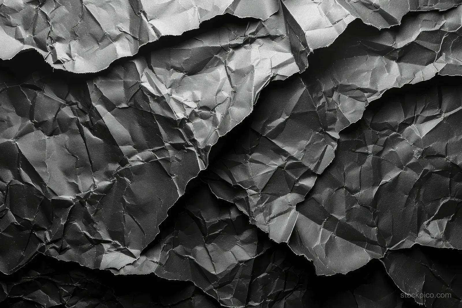 Crumpled black paper fills the frame with layered folds and deep shadowed creases.