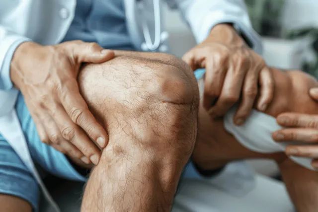 Physiotherapist massaging a patient’s knee during a rehabilitation appointment in a clinic.