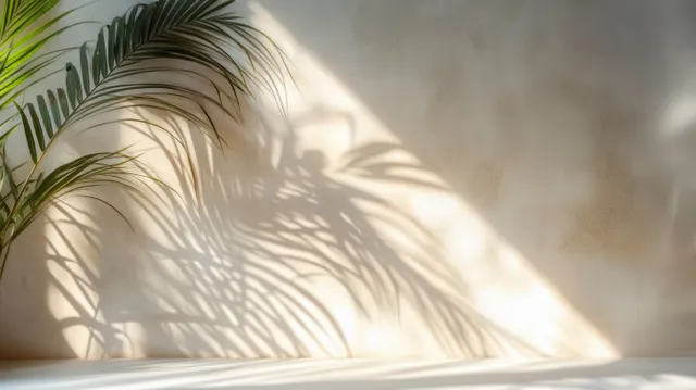 Palm fronds casting intricate leaf shadows across a textured beige interior wall in soft sunlight