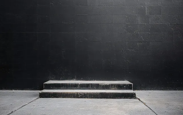 Illuminated black brick wall at night with diffused light on a concrete sidewalk and textured shadows.
