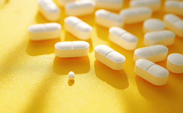 White oval tablets scattered on a bright yellow surface with warm shadows and a smaller pill among them.