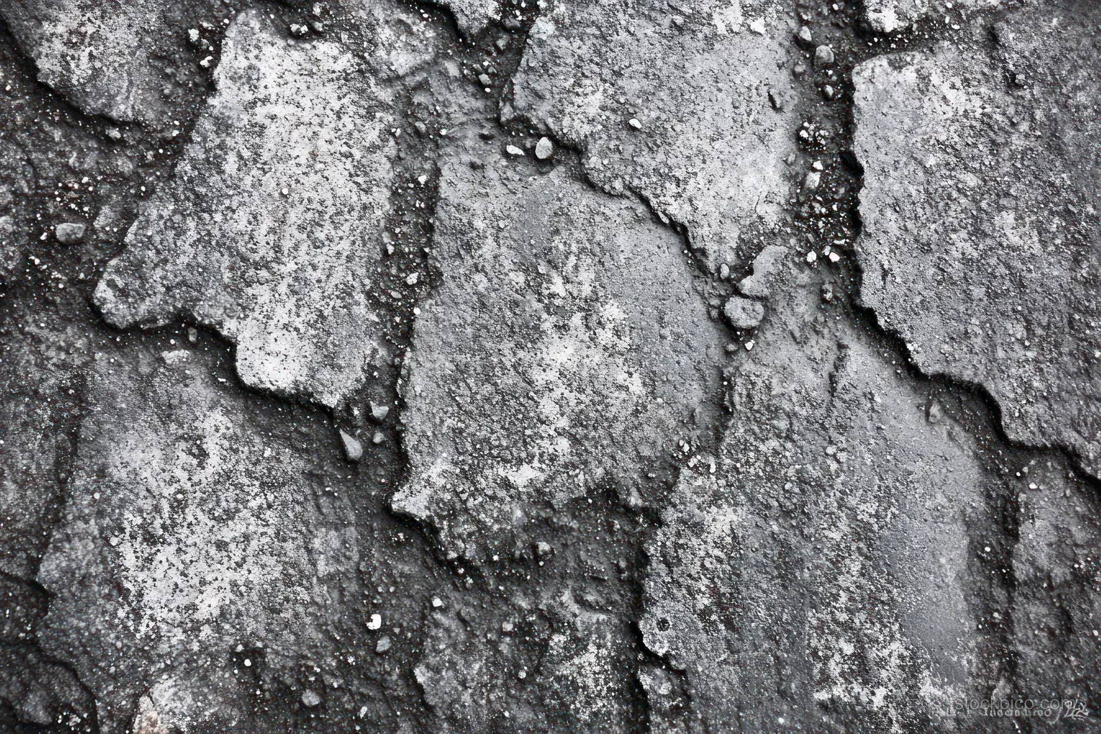 Close-up view of cracked grey asphalt pavement with loose gravel scattered in uneven damaged patches.