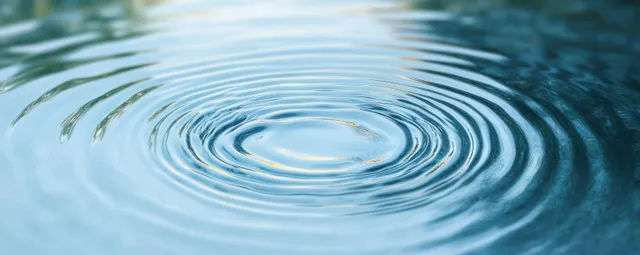 Close-up of concentric ripples spreading across calm blue water surface after a droplet impact.